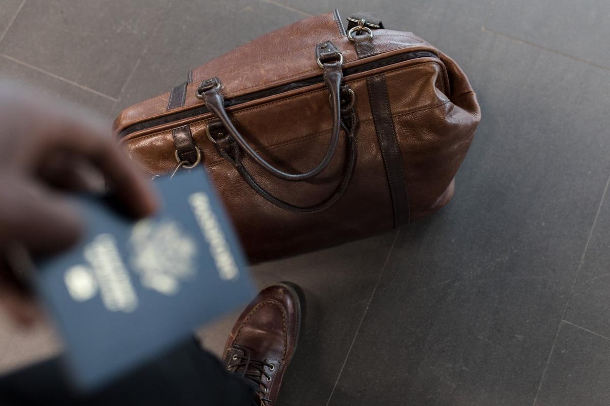 A hand holding a passport and a brown bag on the floor A hand holding a passport and a brown bag on the floor