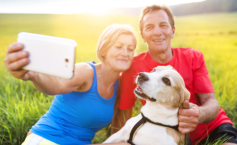 A woman, man, and a dog sat on a field taking a selfie A woman, man, and a dog sat on a field taking a selfie